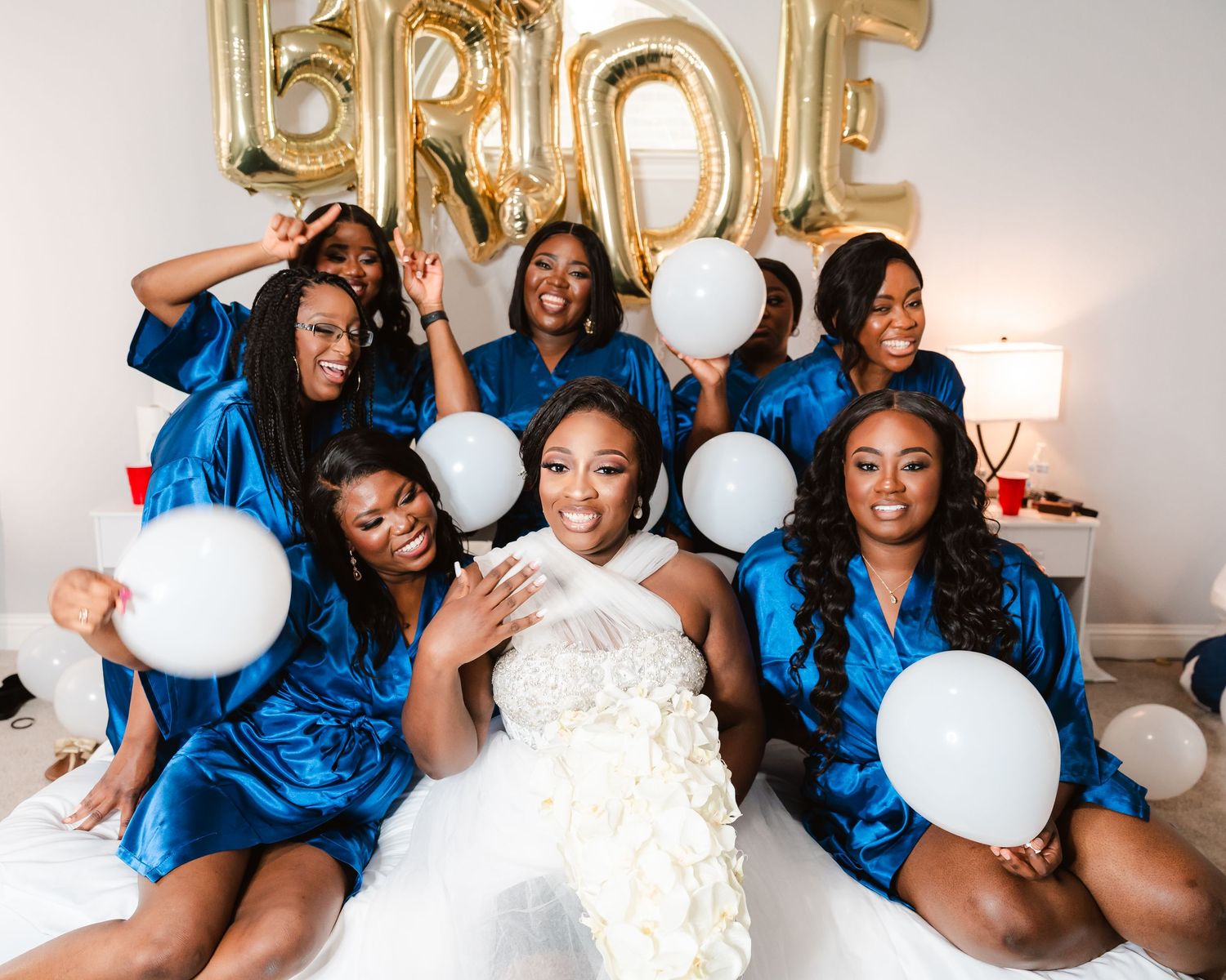 Bridesmaids in royal blue dresses pose playfully with white balloons during wedding photo session.