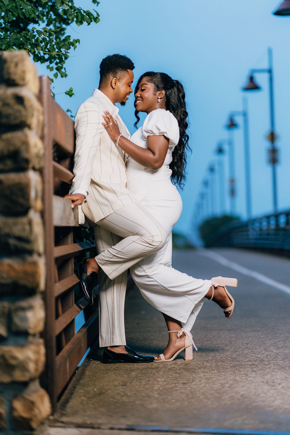 A romantic couple in white clothing performs a dramatic dance dip on a waterfront walkway.