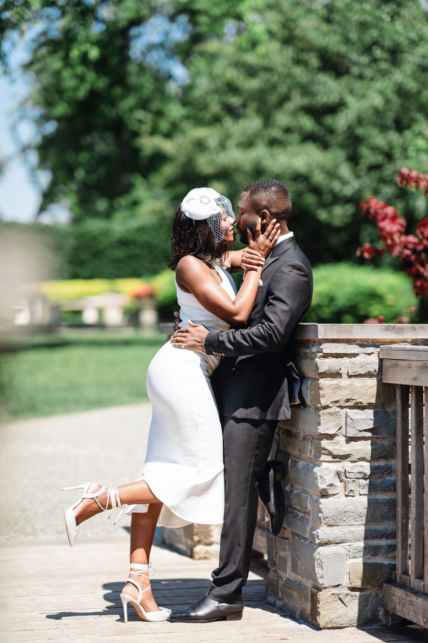 A romantic wedding couple shares intimate moments against a stone wall backdrop in a garden setting.
