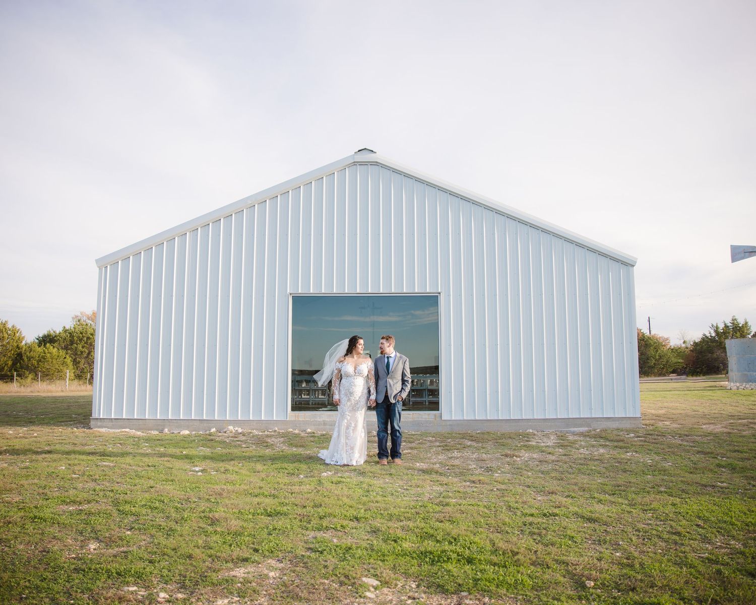 Panoramic view of a white metal barn building in a rural field setting.