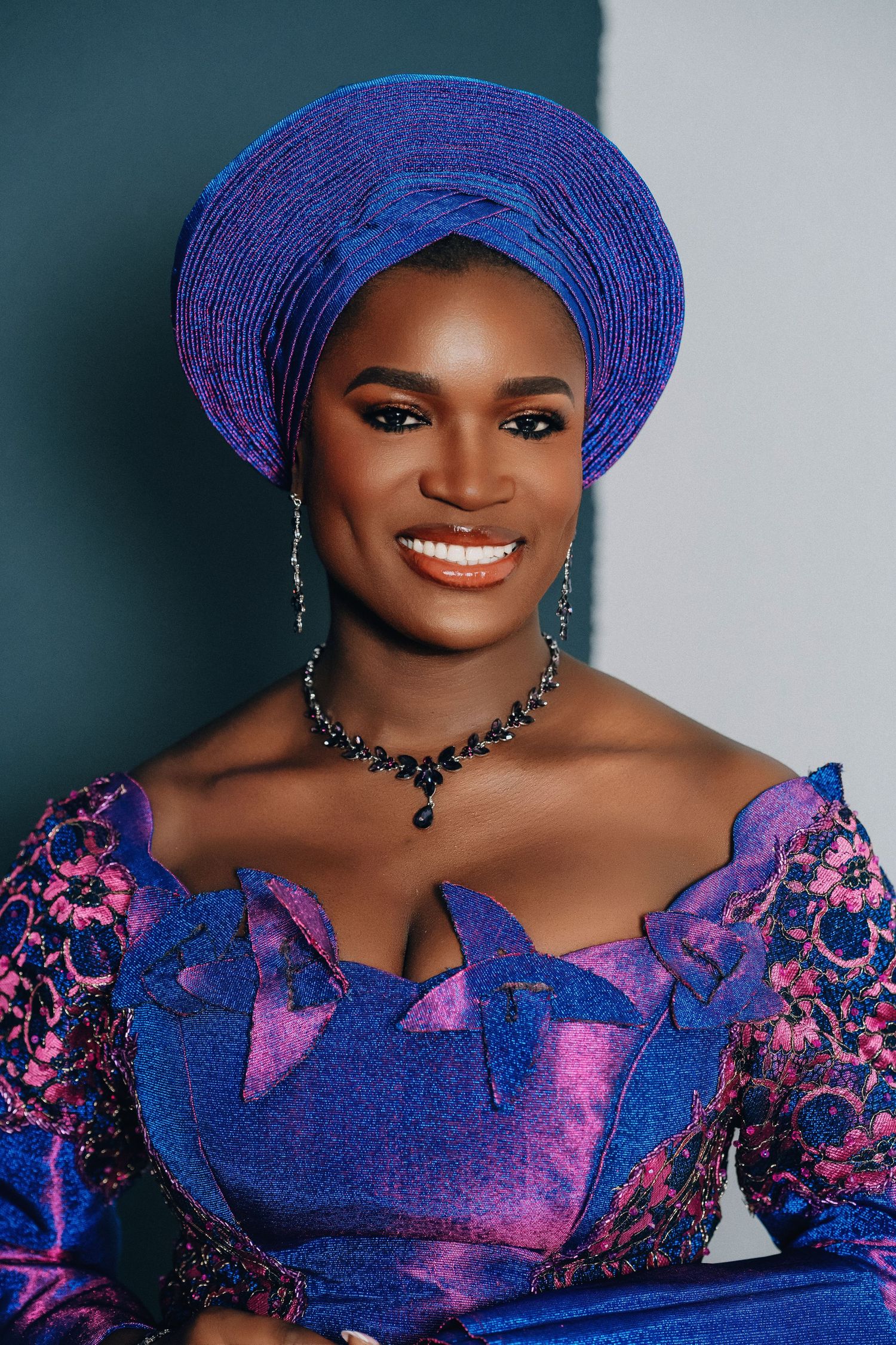 A woman in a stunning royal blue and purple traditional African dress with matching gele headwrap.