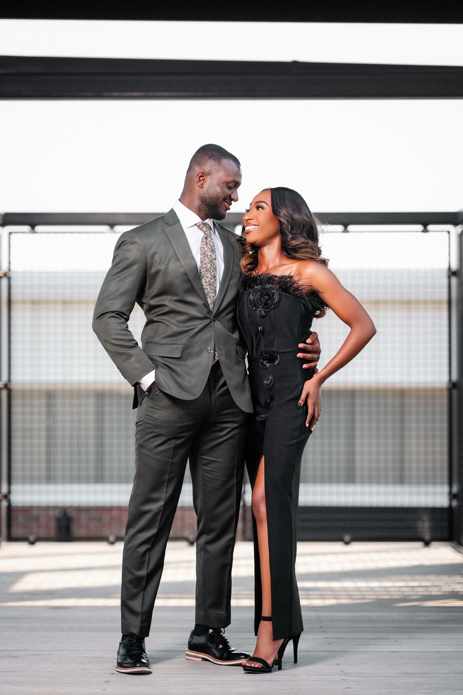 Romantic couple in formal attire share intimate poses during an urban rooftop photoshoot in grey tones.