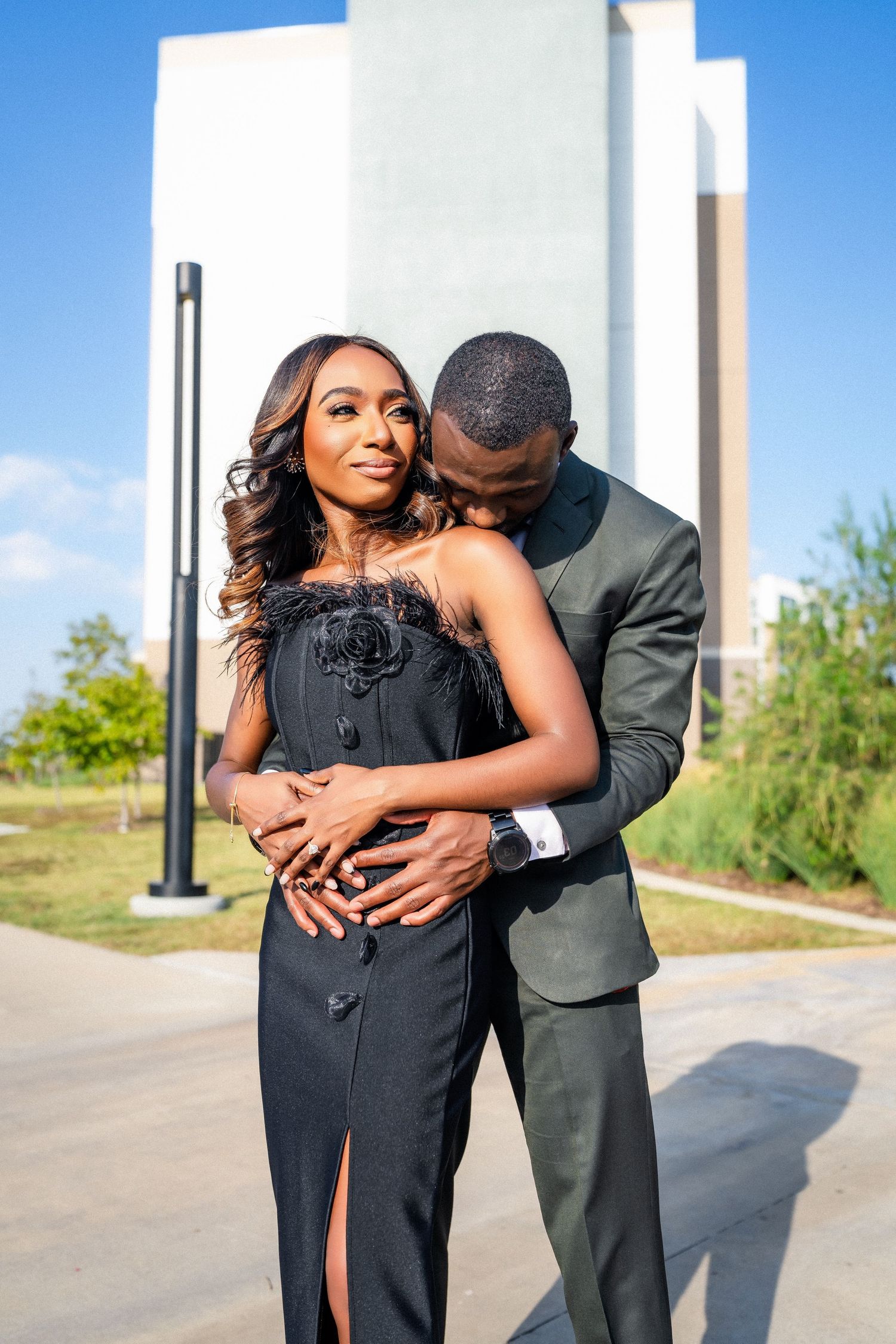 Couple in formal wear embracing against white architectural backdrop.