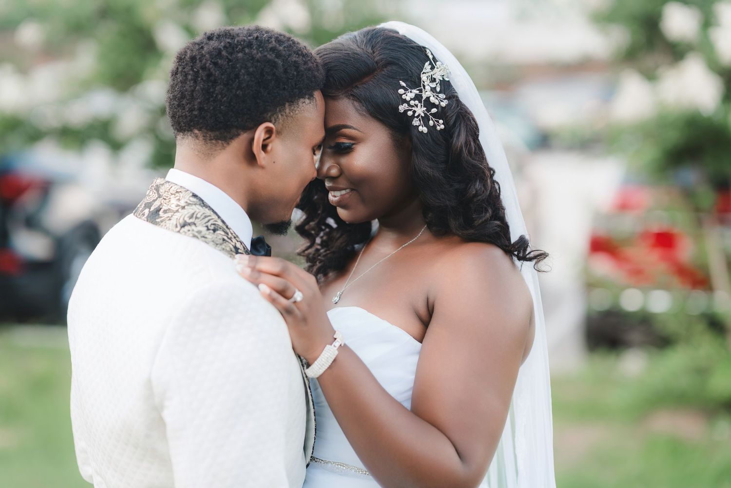 Romantic wedding couple shares intimate moment outdoors surrounded by greenery and floral decor.
