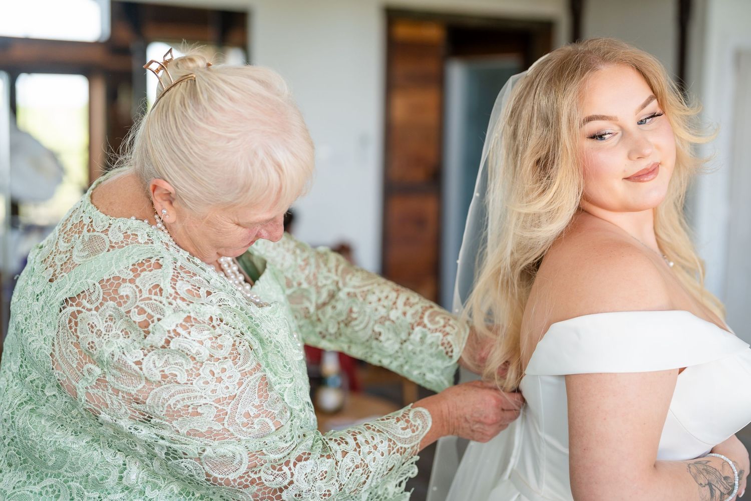 Bride in white dress poses near window with soft natural lighting.