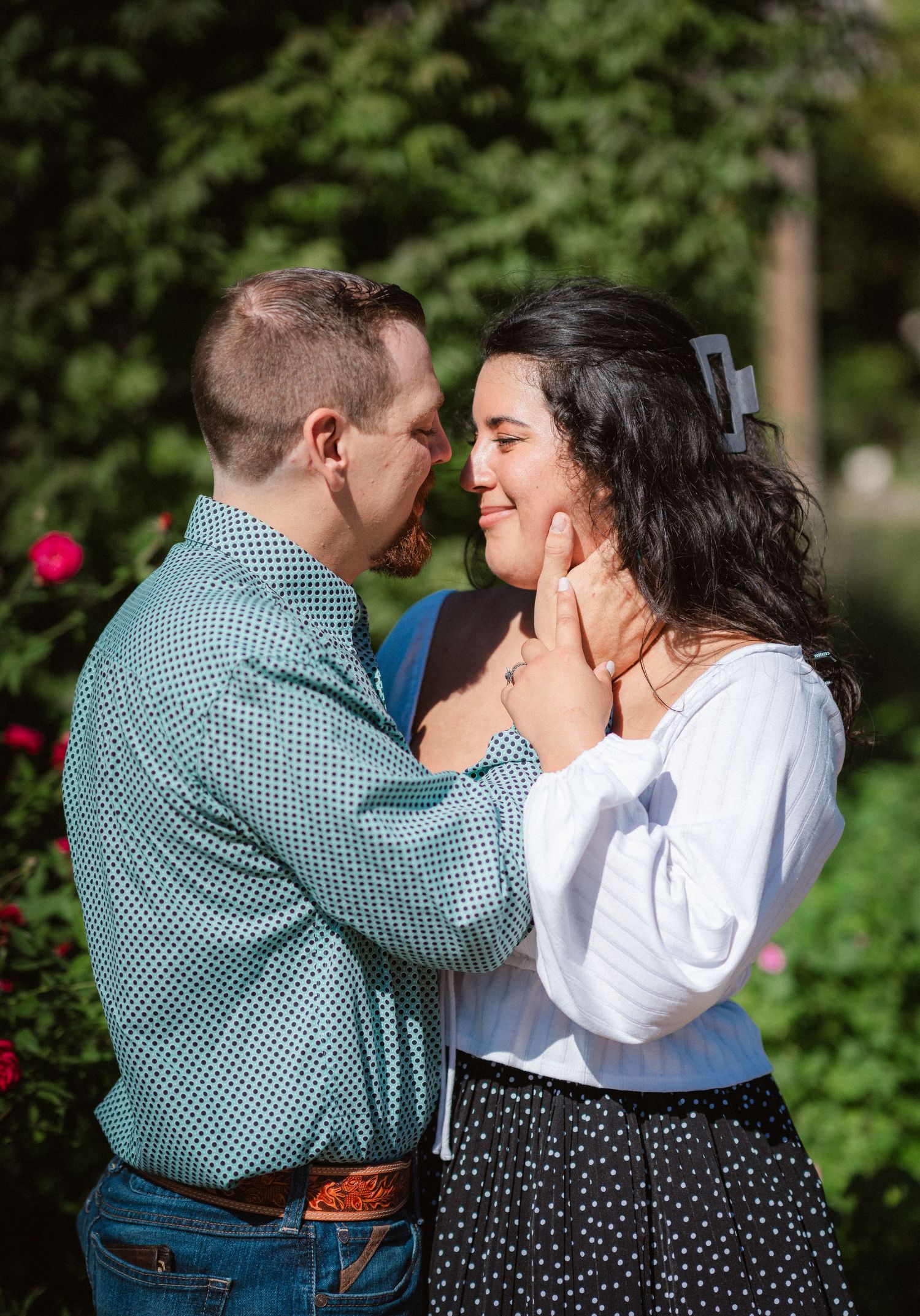 A tender embrace captured in a garden setting with vibrant red flowers and green foliage.