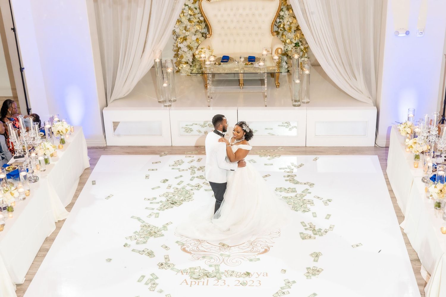 White floral decorations line an elegant indoor wedding aisle with draped fabric and crystal chandeliers overhead.