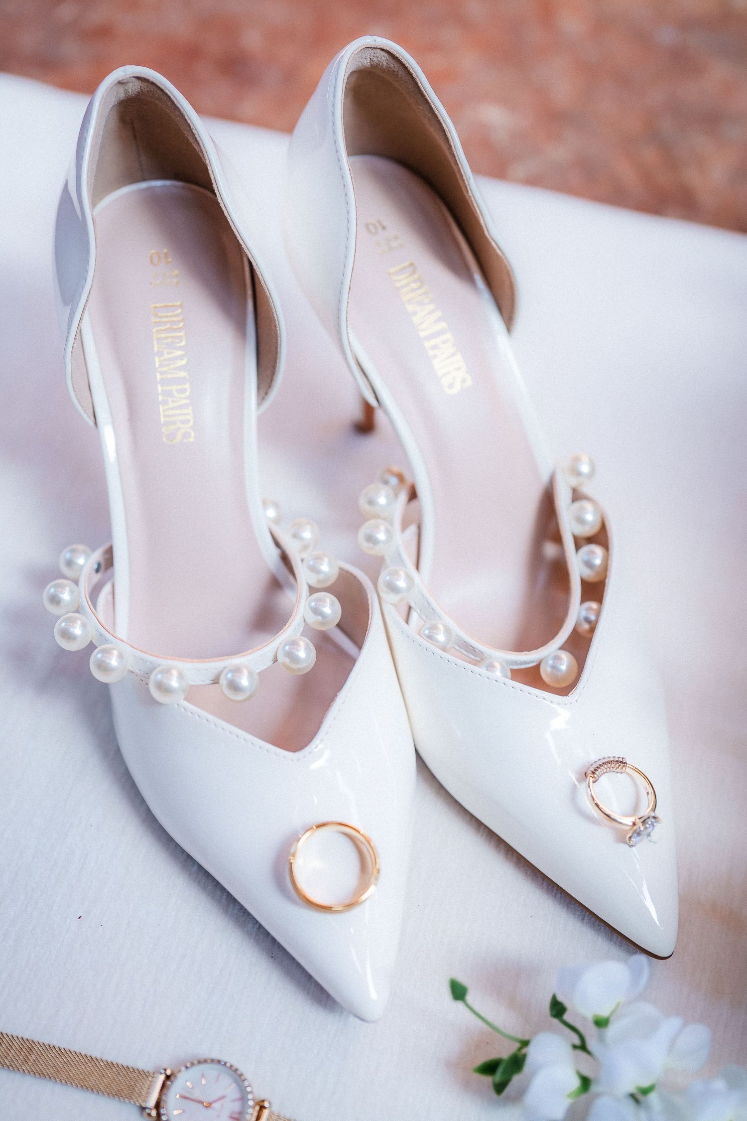 White bridal shoes with pearl details photographed with wedding rings.