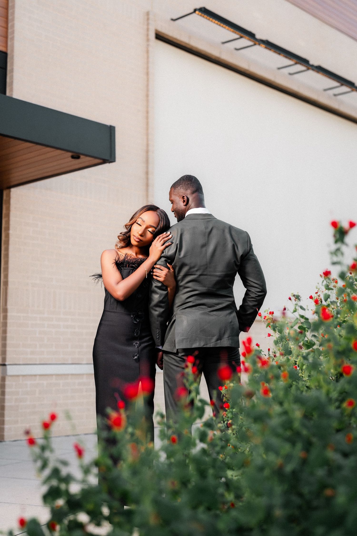 A couple shares intimate moments among red flowers in an outdoor engagement photoshoot.