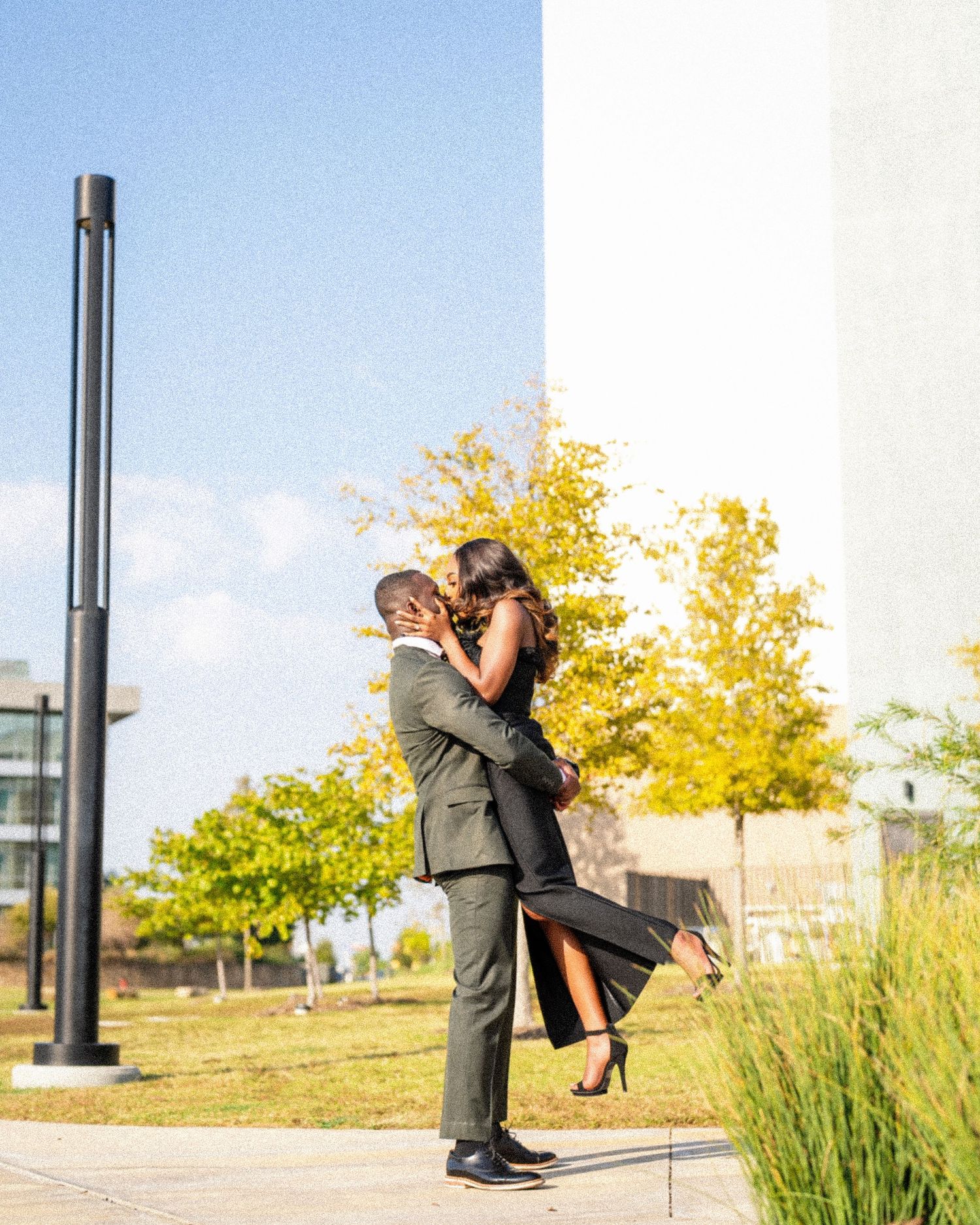 Couple shares joyful embrace outdoors with autumn trees in background.