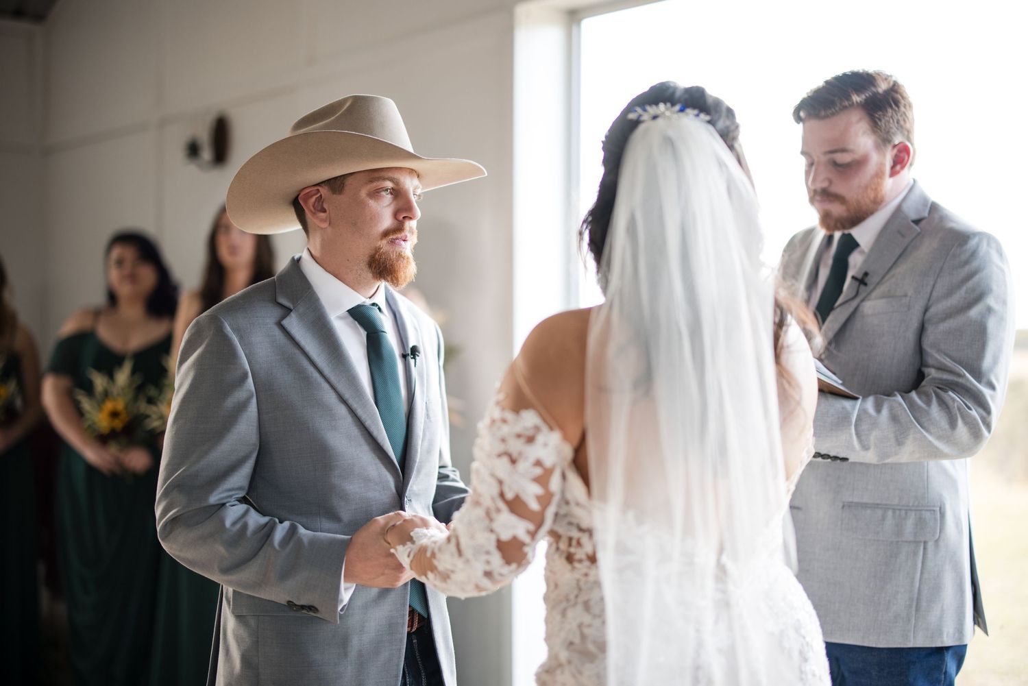 An indoor wedding ceremony moment with western style featuring a grey suit and cowboy hat.