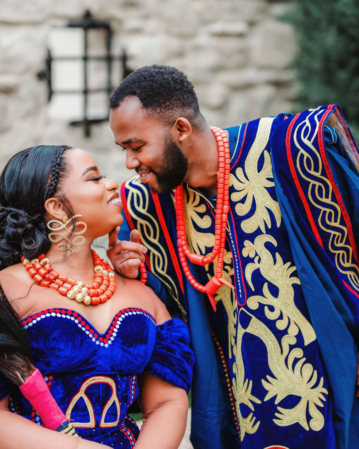 A couple shares intimate moments wearing vibrant blue and red traditional outfits with ornate gold patterns.
