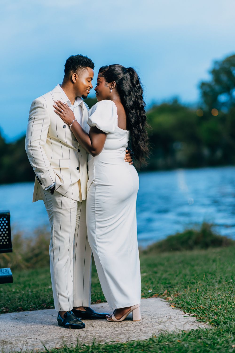 Romantic couple in white outfits share an intimate moment by a lake during a photo session.