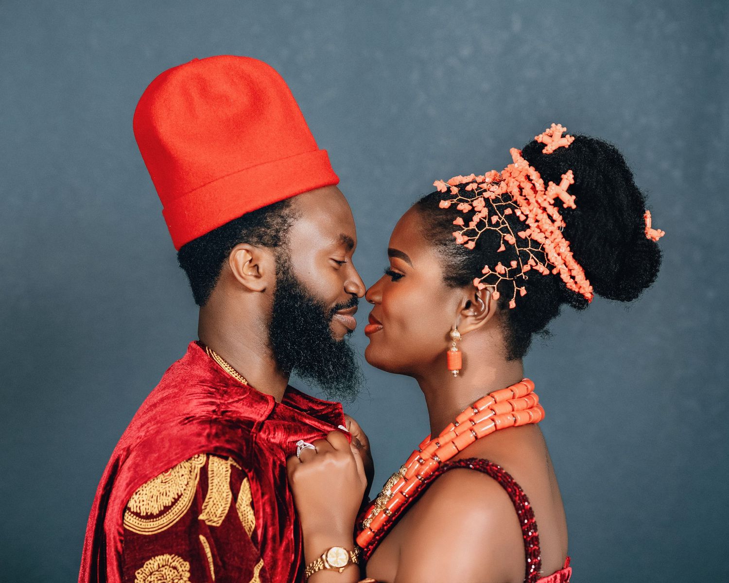 A romantic couple in traditional African wedding attire share an intimate moment against a dark backdrop.