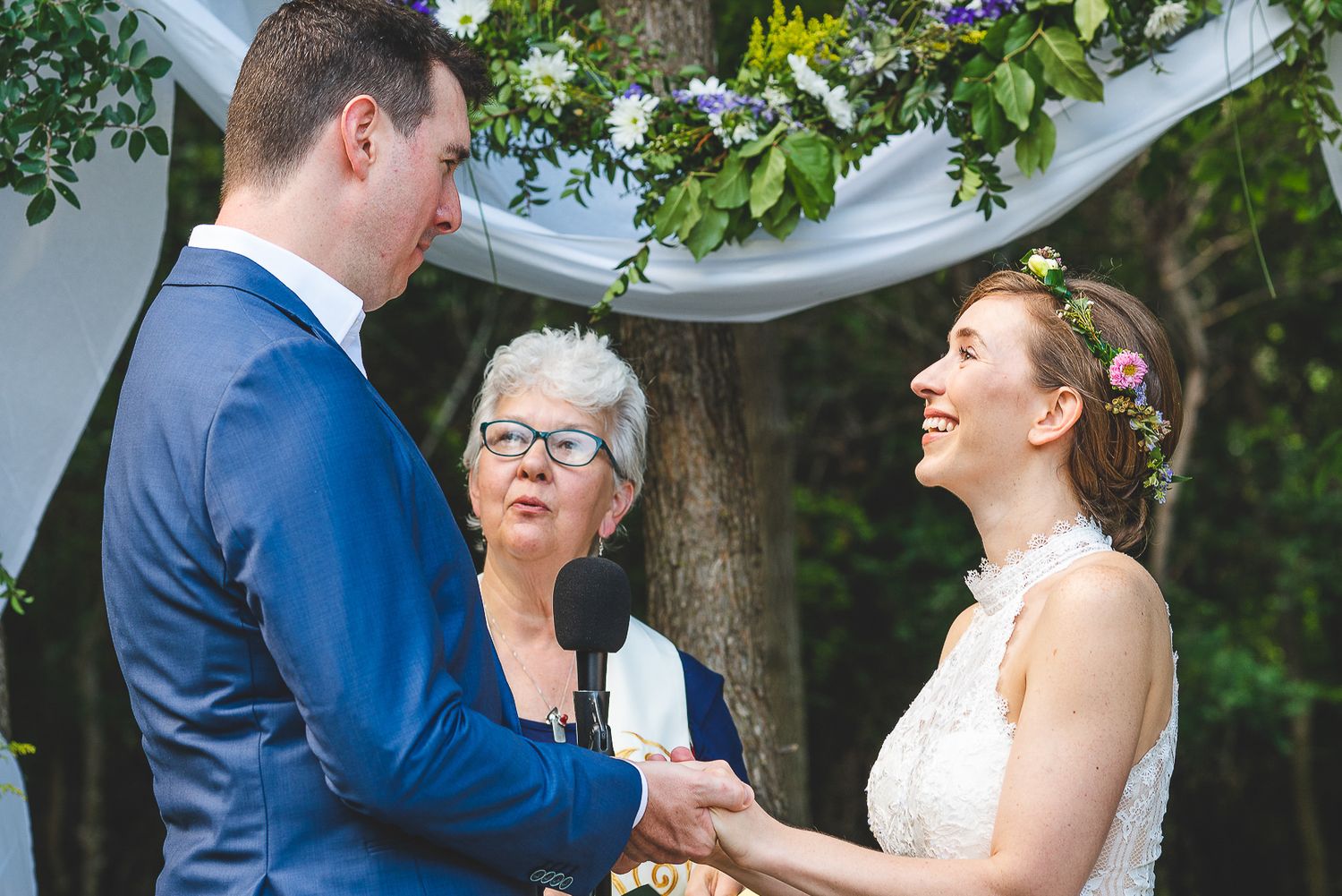 Outdoor wedding ceremony under white fabric draping with greenery and natural lighting.
