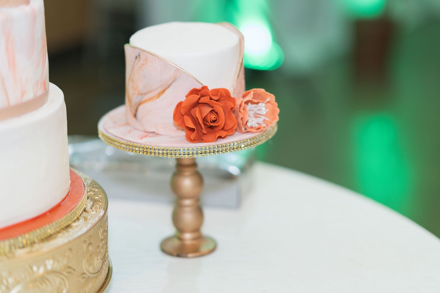 Wedding cake detail shot with coral floral decorations and green lighting in the background.