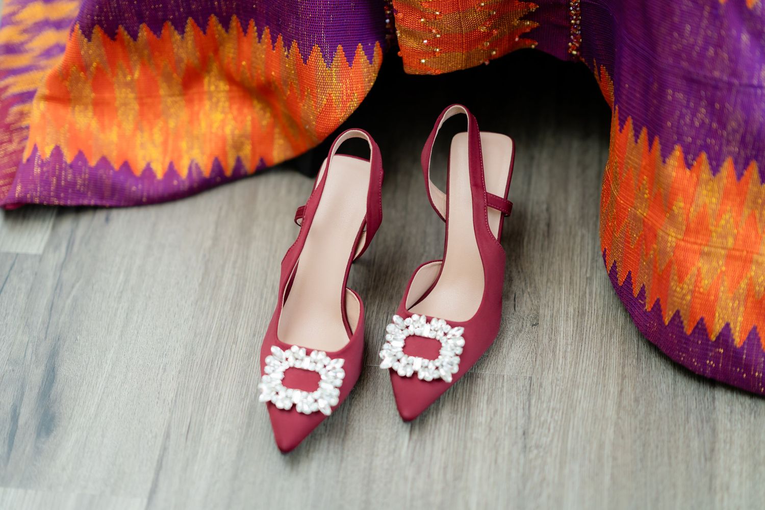 Close-up of pink high heels with lace details against purple and orange fabric.