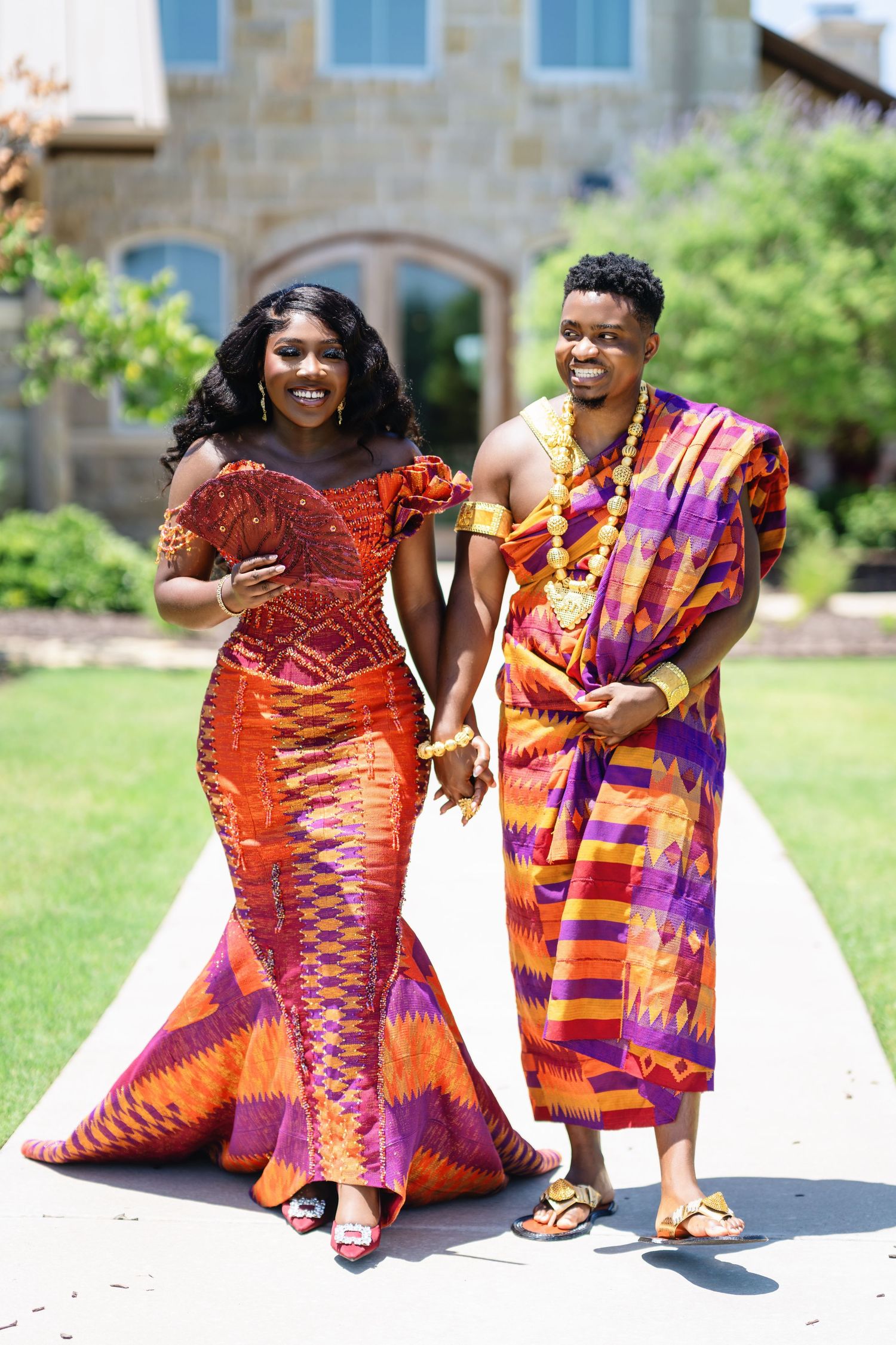 Couple in matching African print outfits posing together on stone patio.