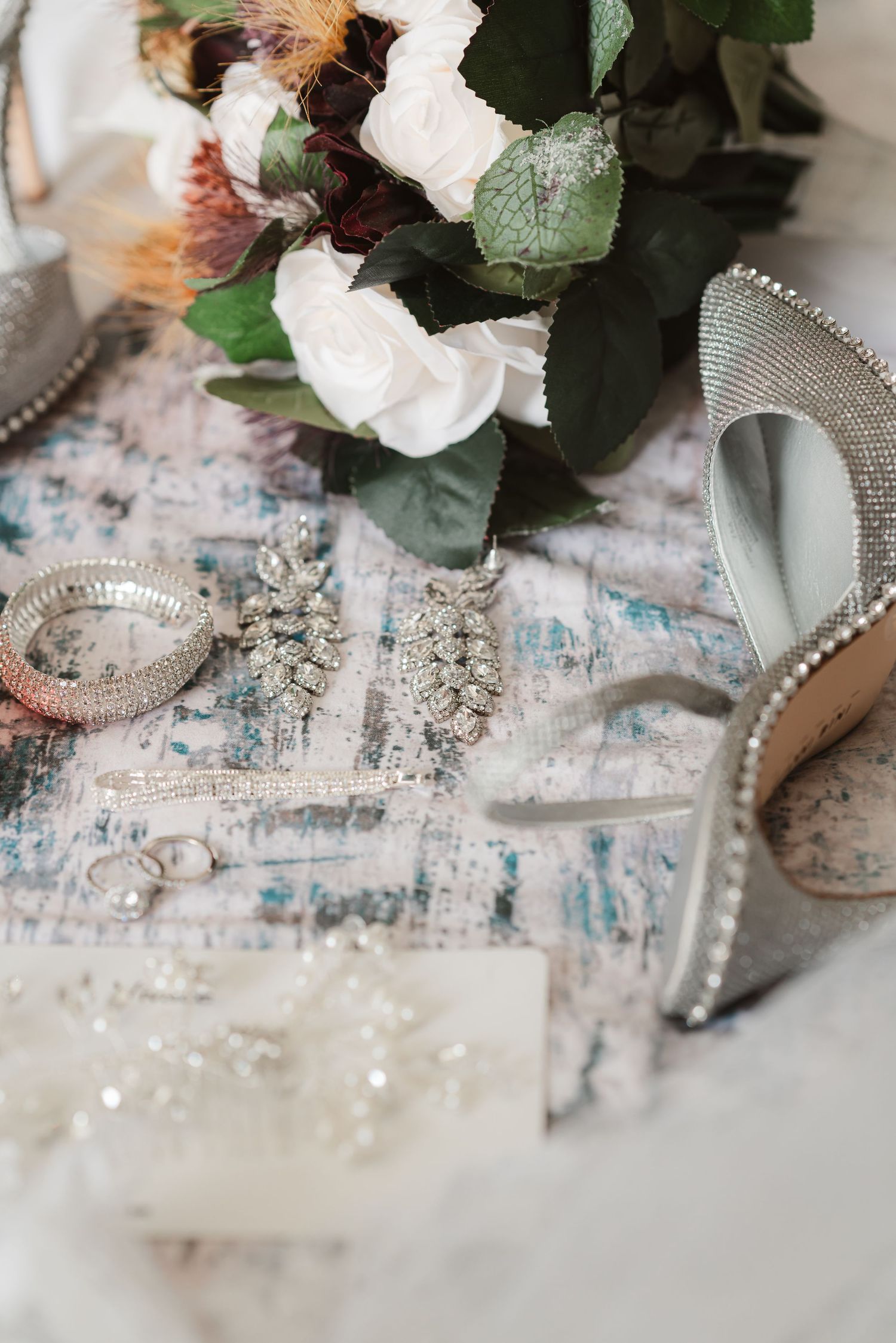 Wedding accessories including floral arrangements and crystal details laid out on a textured surface.