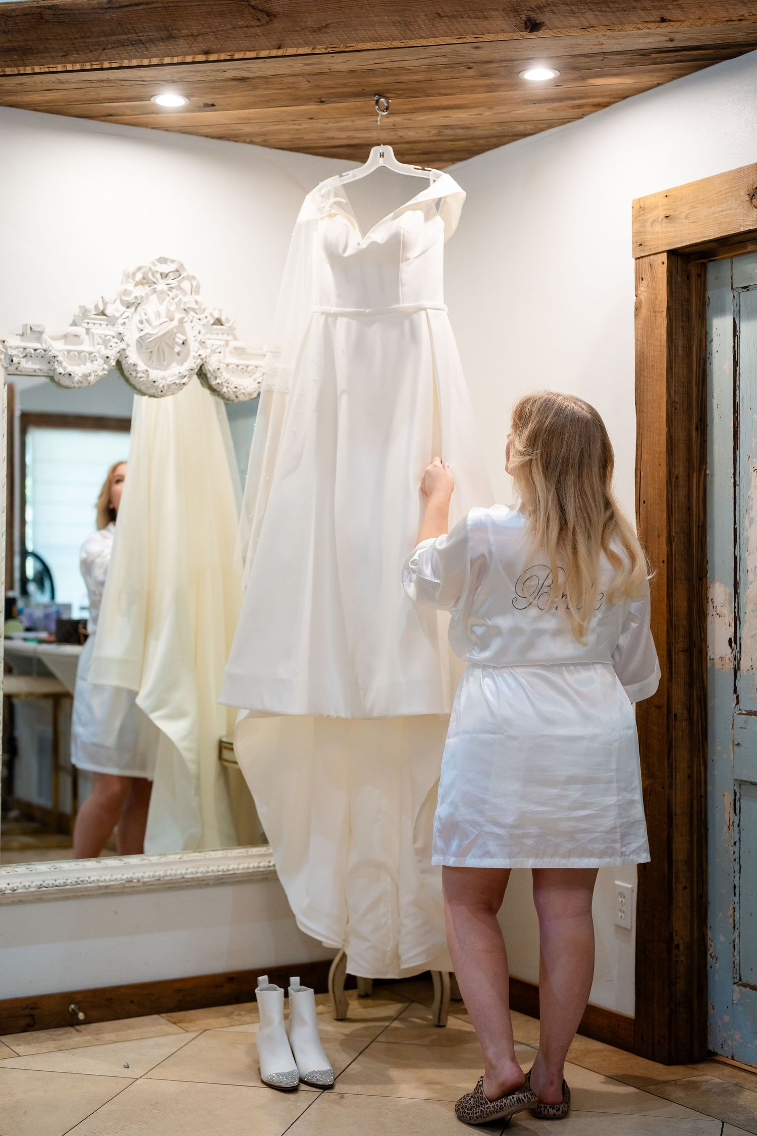 Wedding dresses displayed in a rustic dressing room with wooden ceiling and white walls.