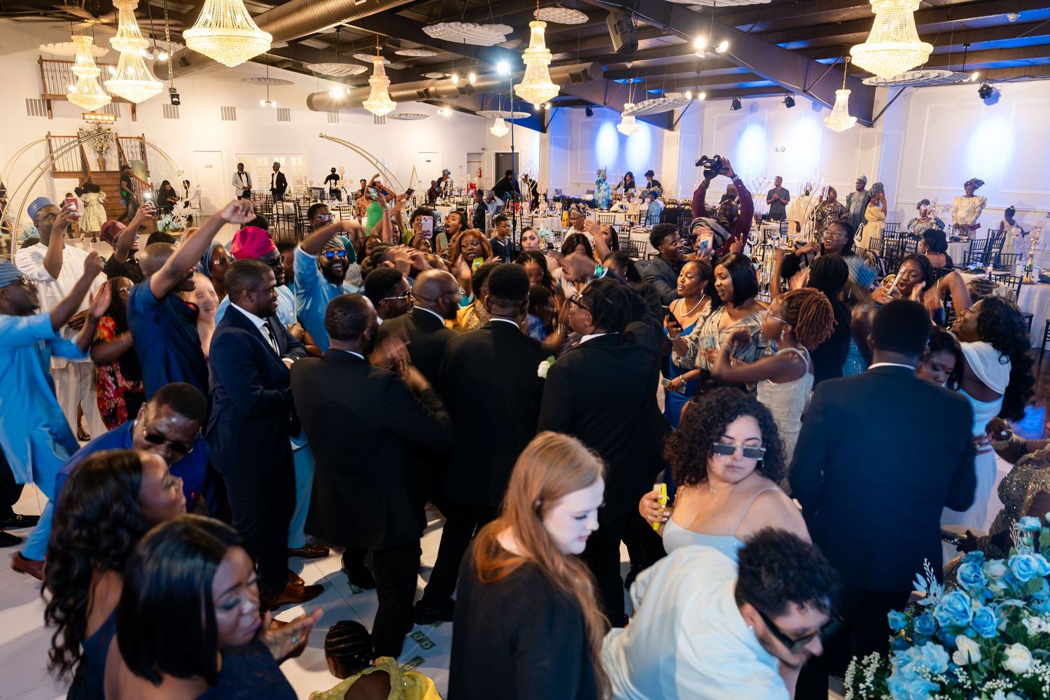 A crowded wedding reception with guests dancing under crystal chandeliers.