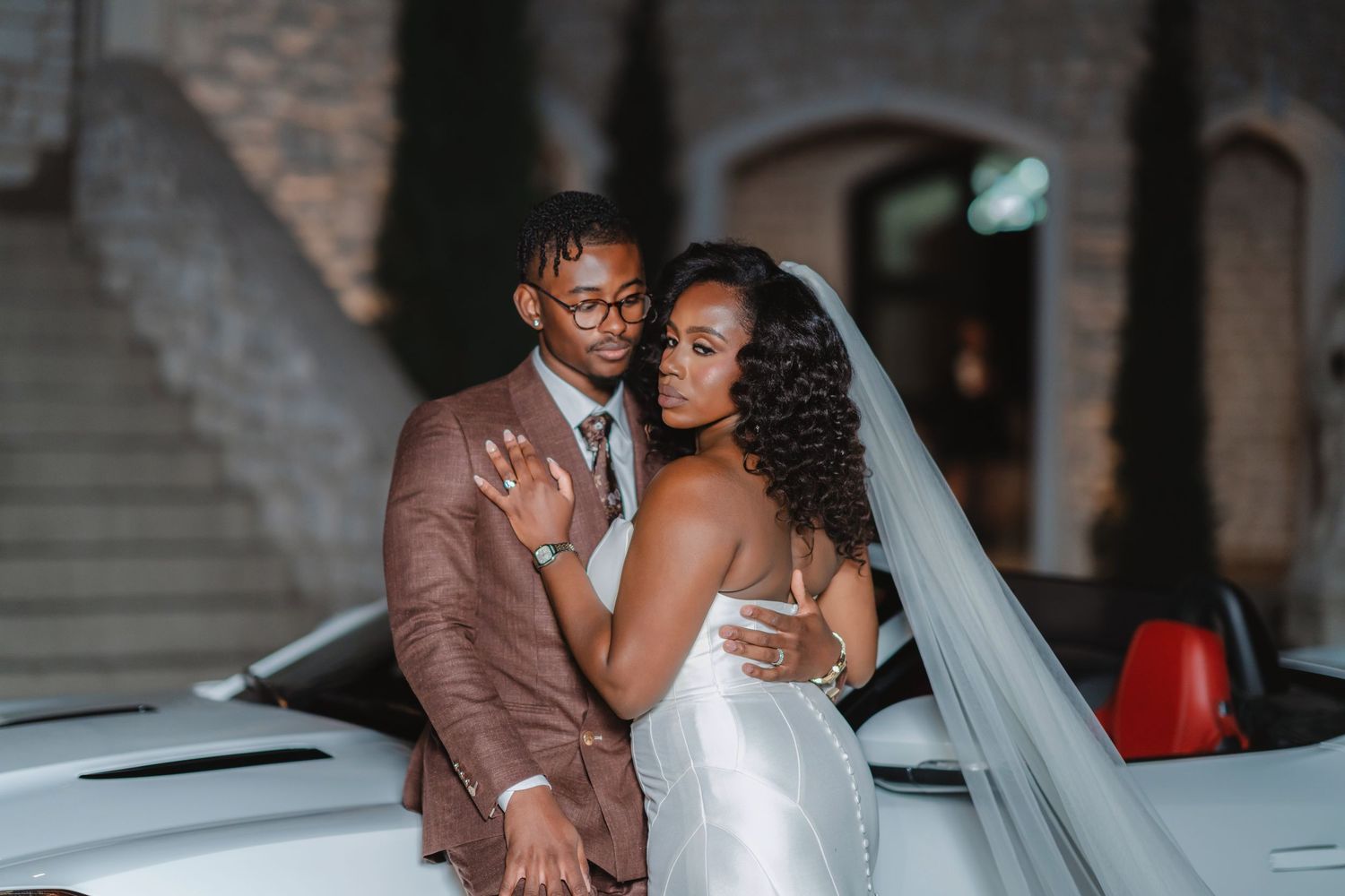 Wedding couple shares an intimate moment near a classic car at their reception.