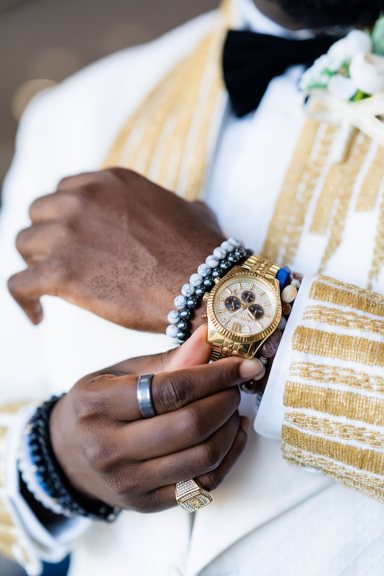 Close-up of hands wearing beaded bracelet and gold watch with white and gold formal sleeve.