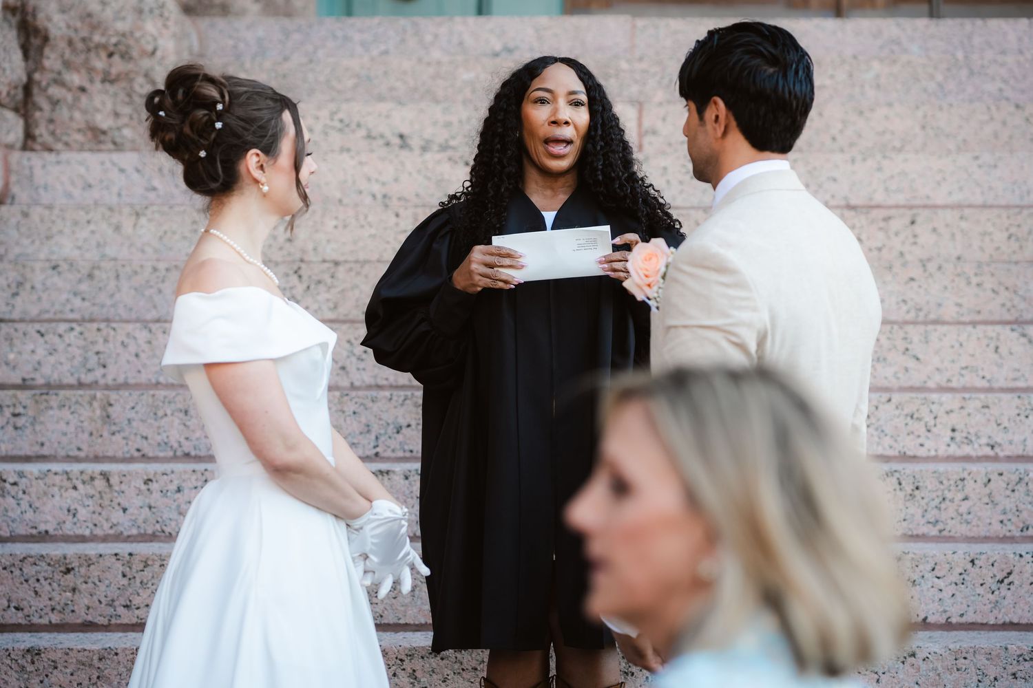 An outdoor wedding ceremony with an officiant and couple on stone steps.