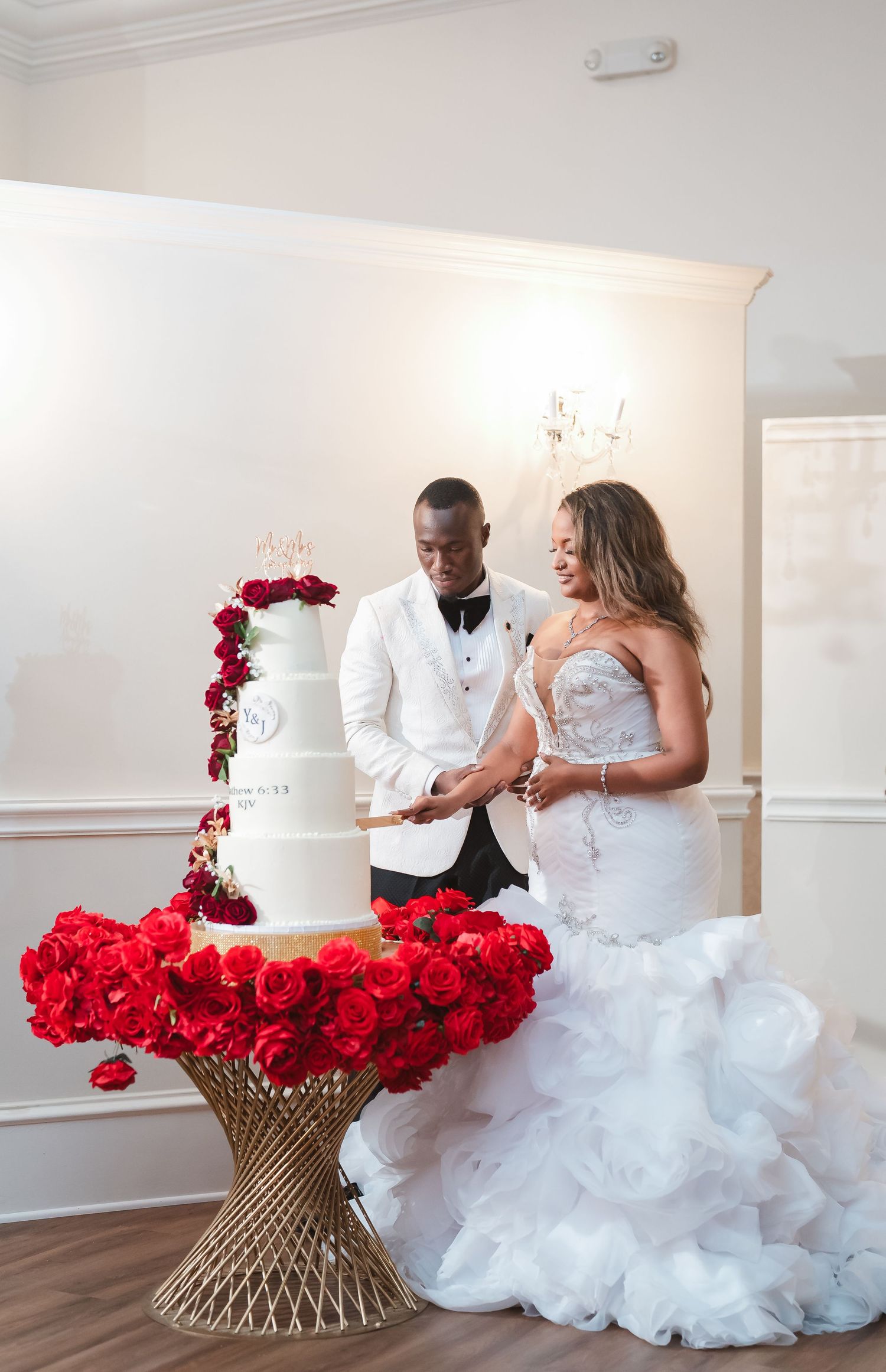 A couple cuts their elegant white wedding cake decorated with cascading red roses.