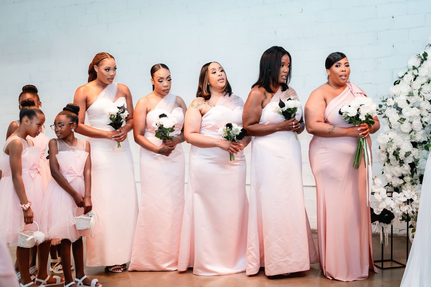 Bridesmaids in matching light pink dresses standing in a row holding bouquets.