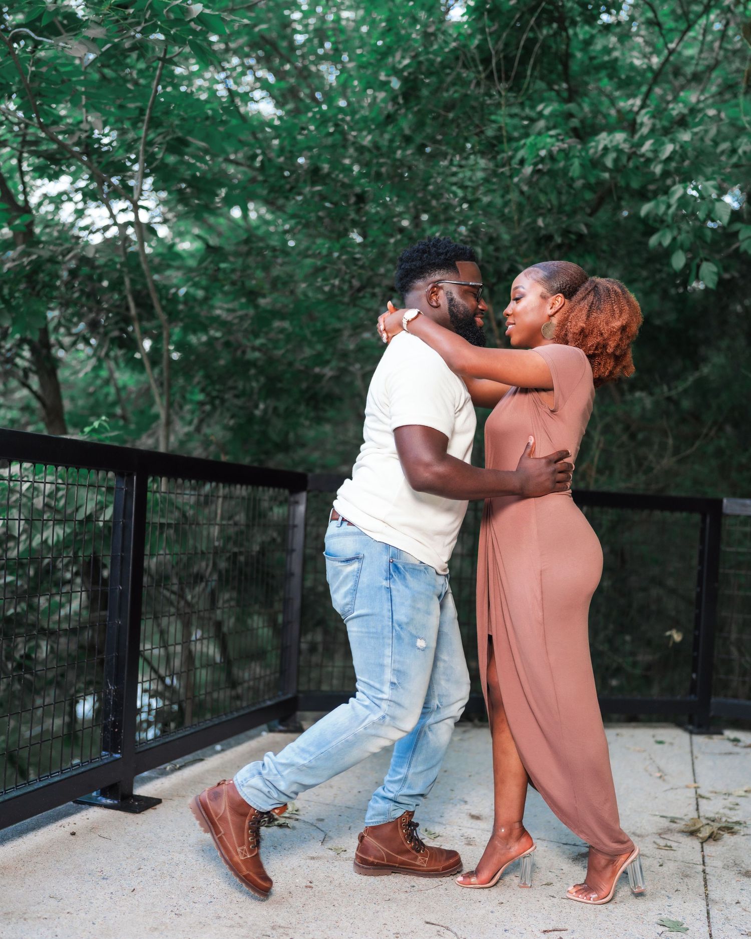 A couple shares a playful moment on a bridge walkway surrounded by greenery.