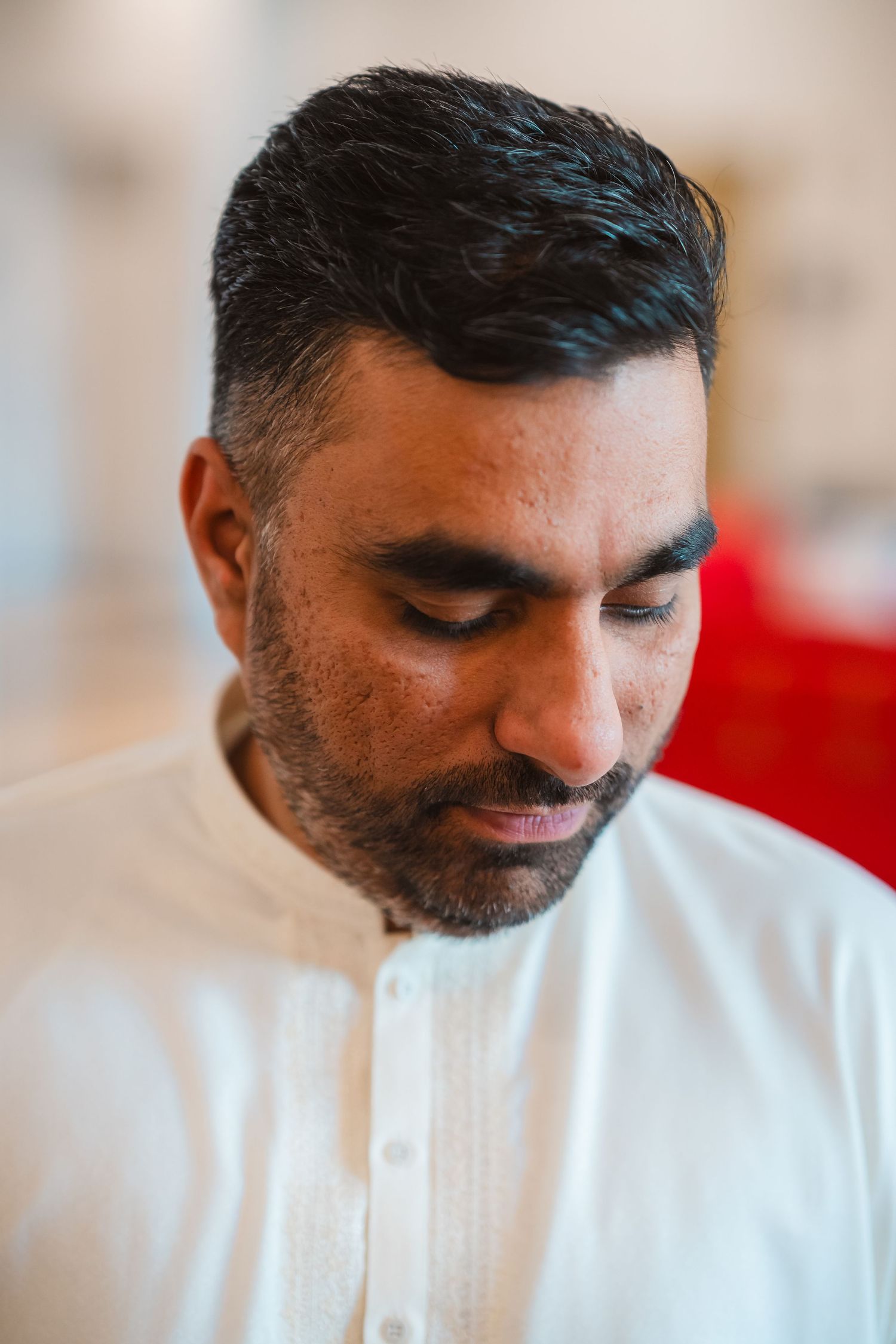 Traditional South Asian groom wearing a crisp white embroidered kurta in a formal portrait setting.