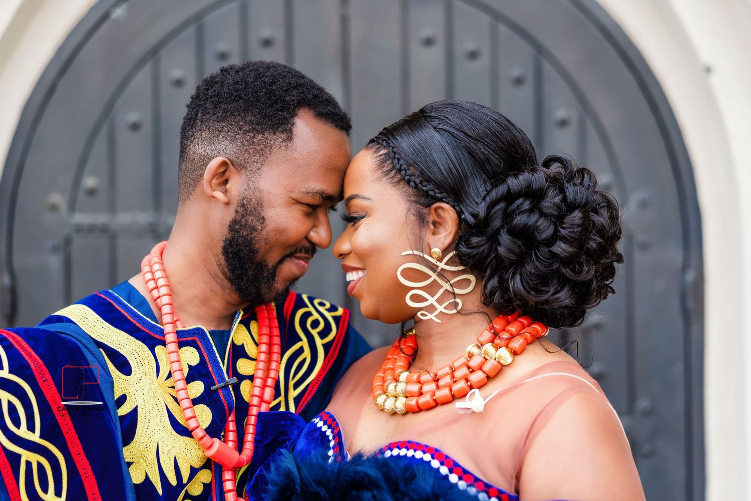 A couple in traditional African attire shares an intimate moment against an arched doorway background.
