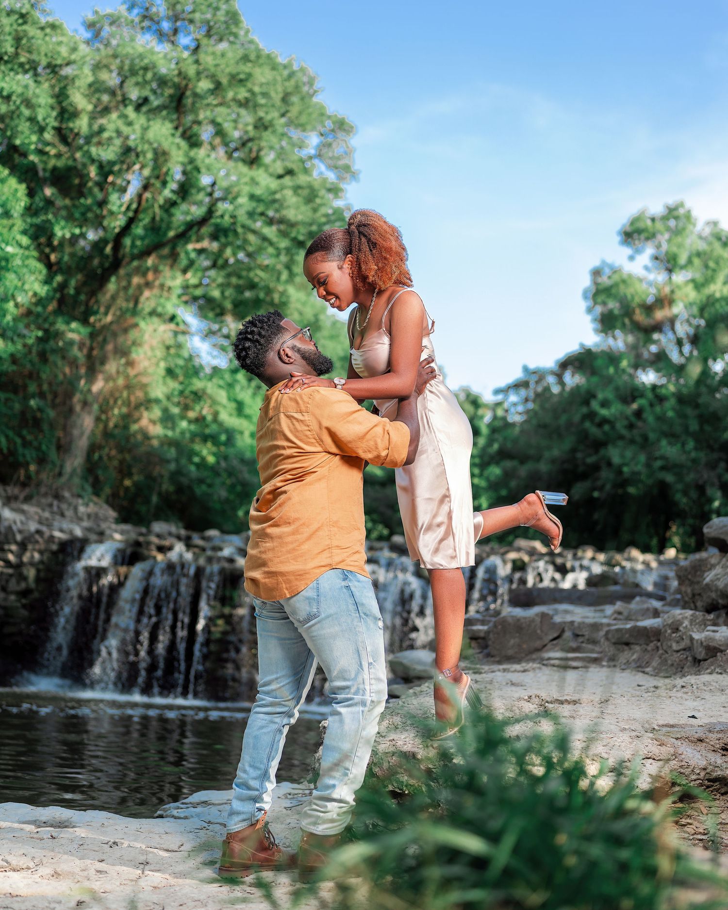 A couple shares romantic moments by a scenic waterfall, captured in a series of engagement-style photos in nature.
