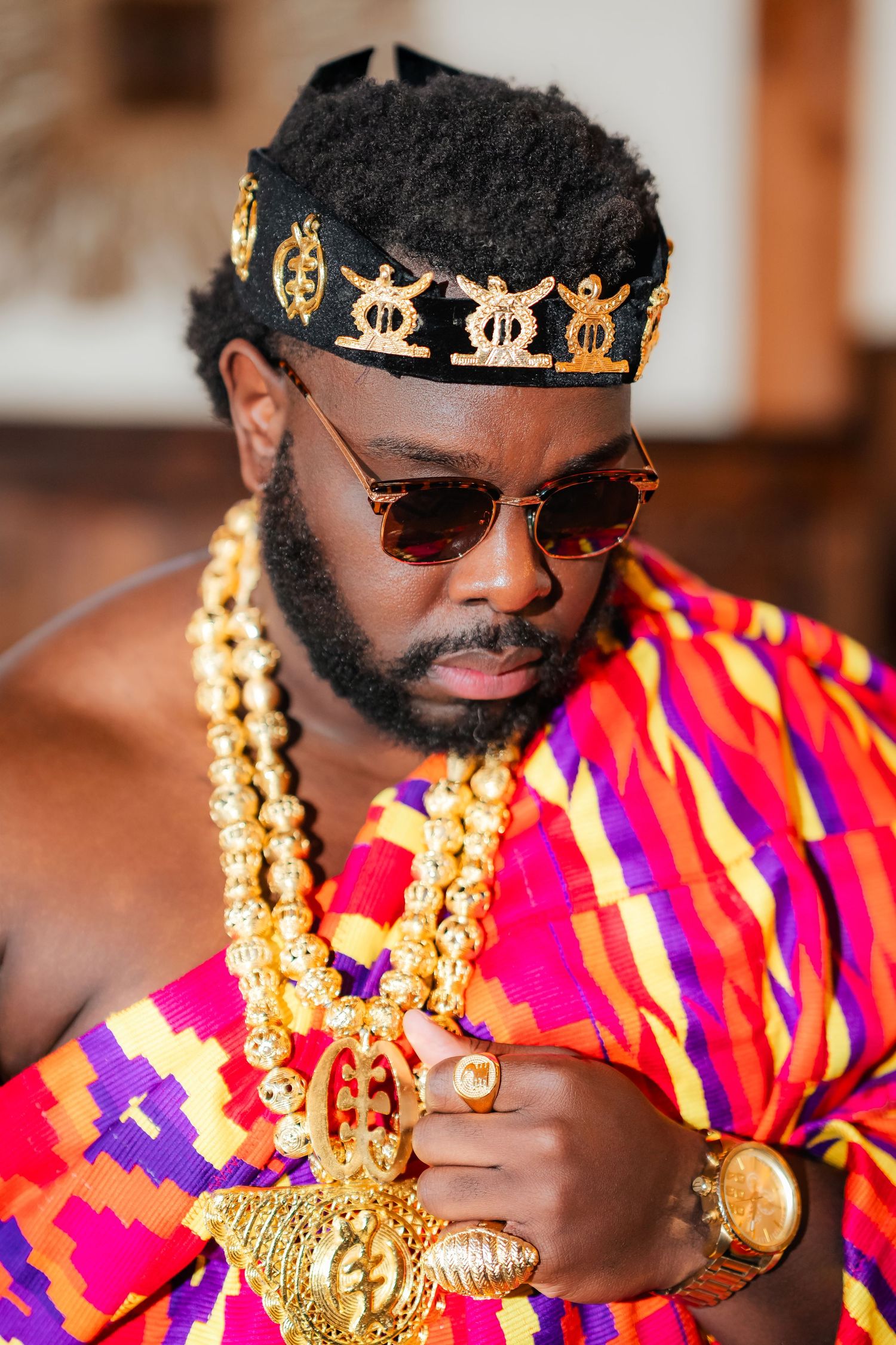 Traditional African attire featuring vibrant red and pink kente cloth and gold accessories in a cultural celebration.