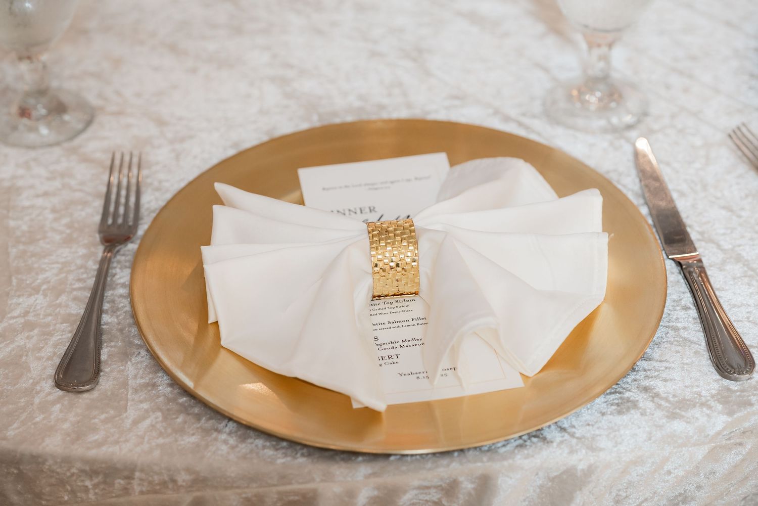 Place settings with gold charger plates and white napkins arranged on an elegant dining table.