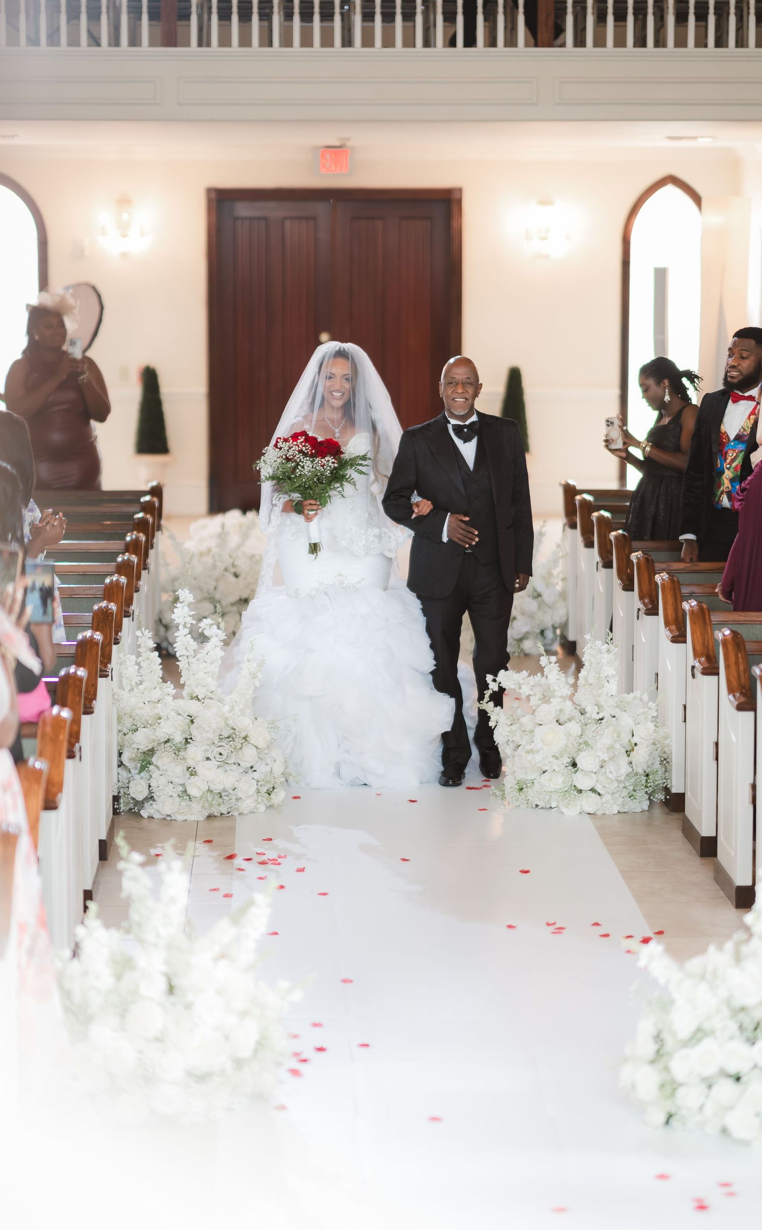 Church aisle decorated with white floral arrangements and rose petals for a wedding ceremony.