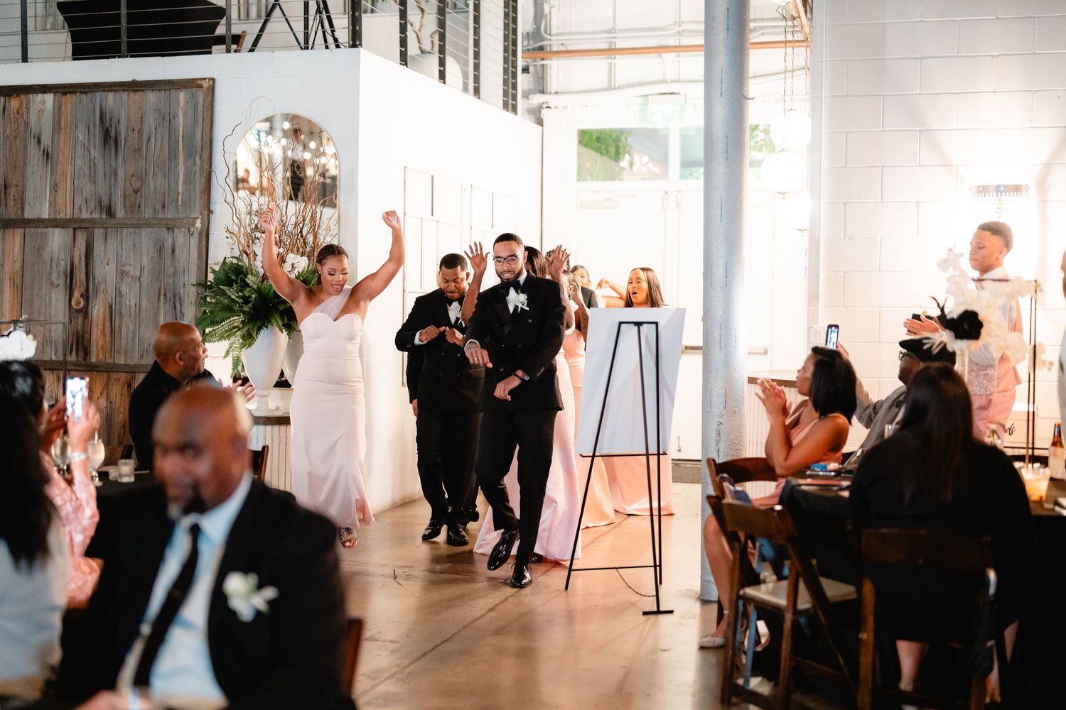 Wedding guests dancing and celebrating in a bright, modern white venue space.