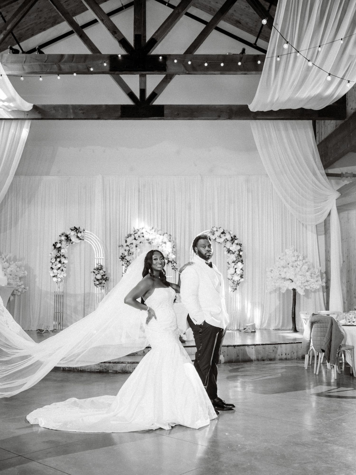 Elegant wedding couple dances in a beautifully decorated white reception hall with floral arches.