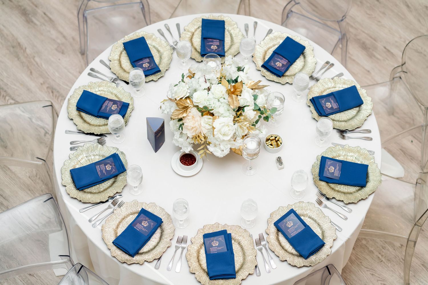 Elegant wedding reception table settings with blue napkins and white floral centerpieces on round tables.