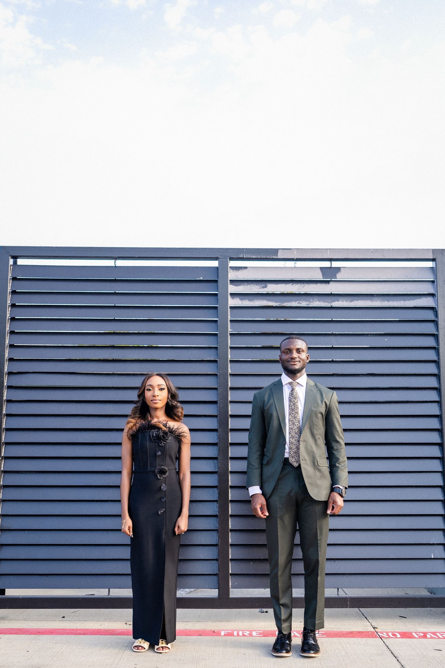 Formal couple poses against modern blue architectural backdrop.