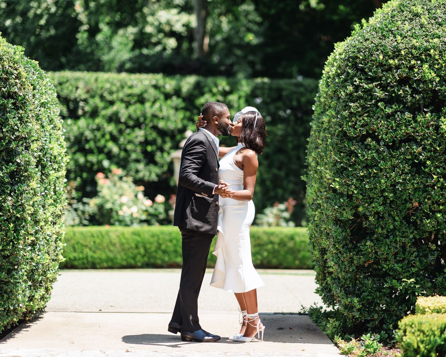 A romantic moment between a couple in formal wear surrounded by manicured garden hedges.