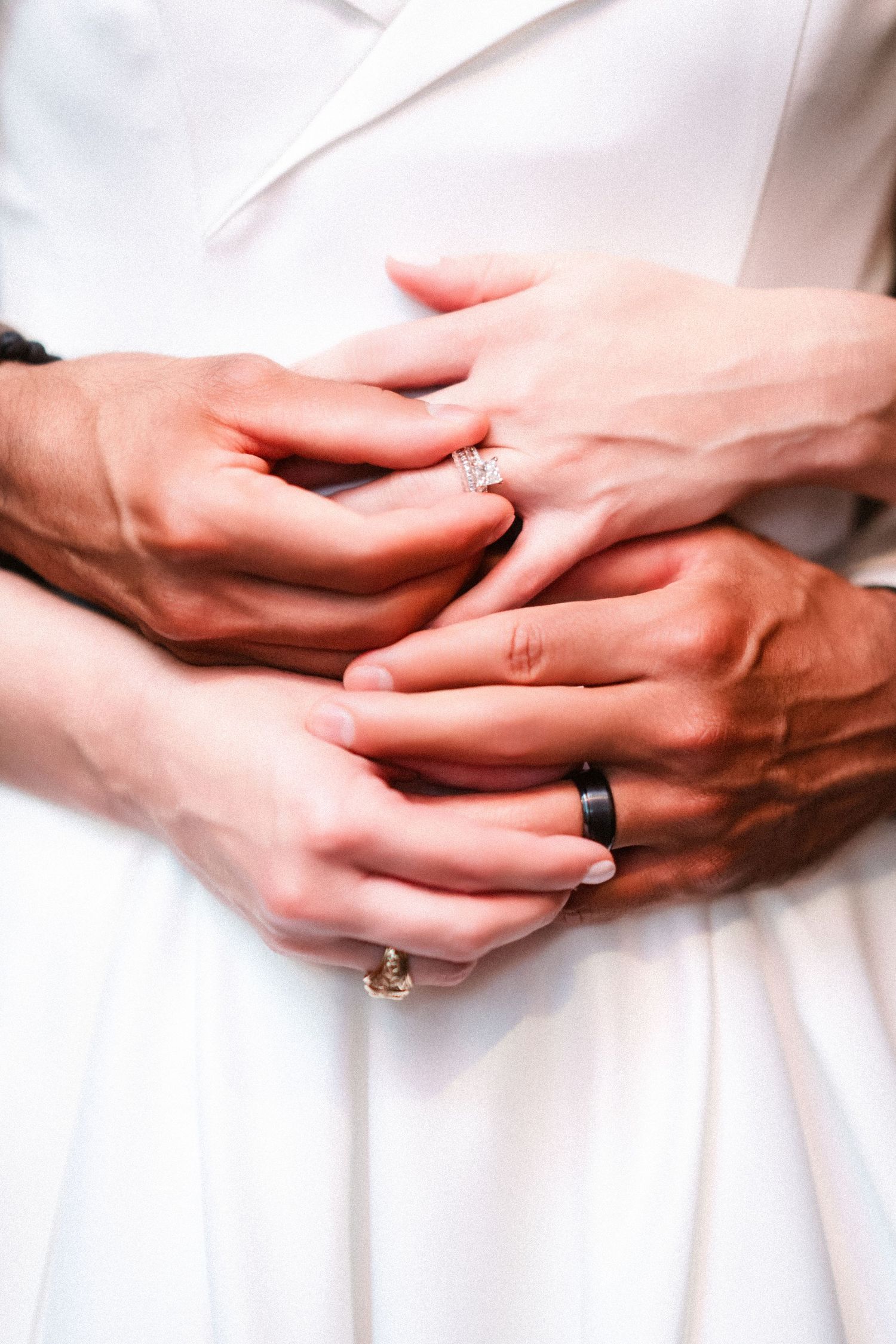 Close-up of hands with wedding rings intertwined against white fabric background.