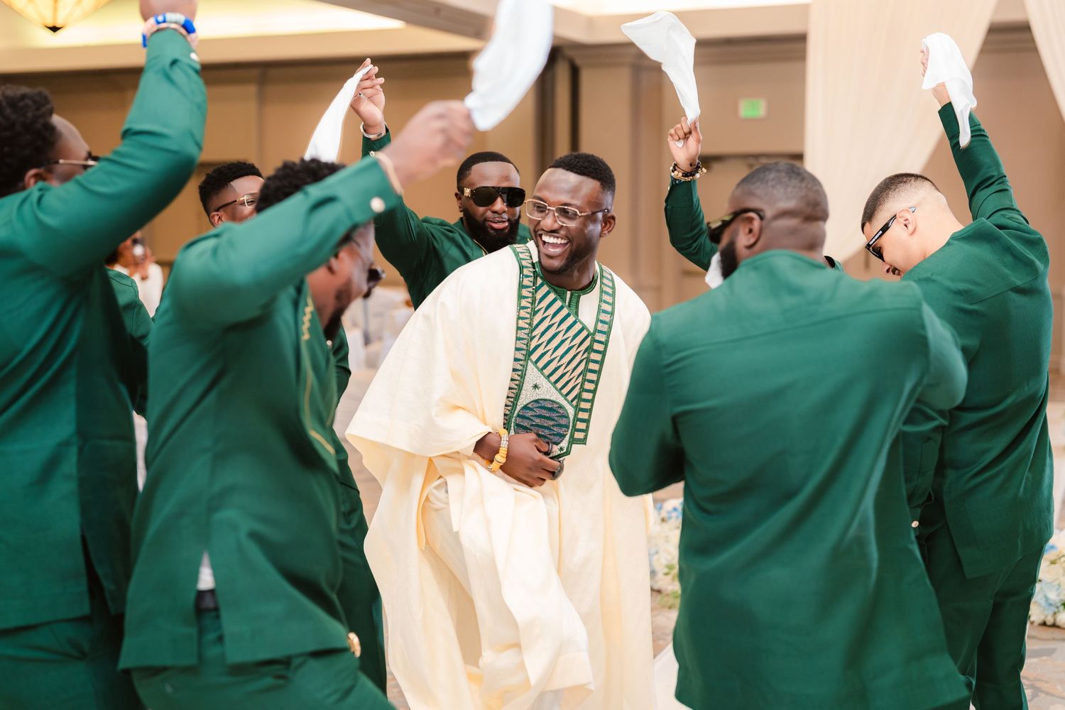 Groomsmen in green suits celebrate with the groom in traditional white attire.