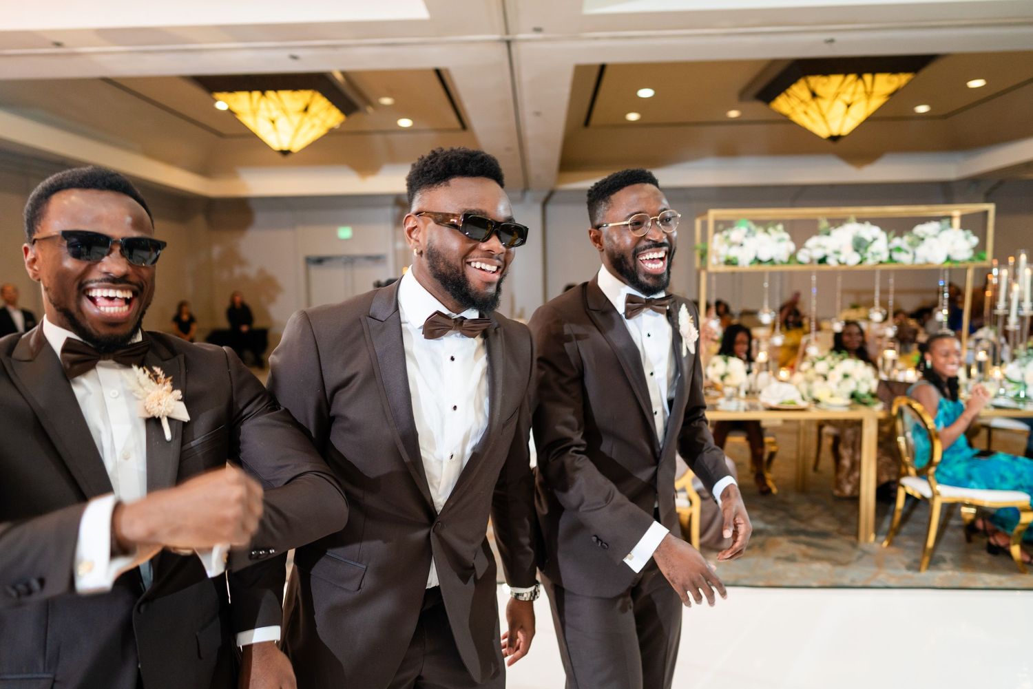 Wedding party members in dark suits strike fun poses during reception celebrations.