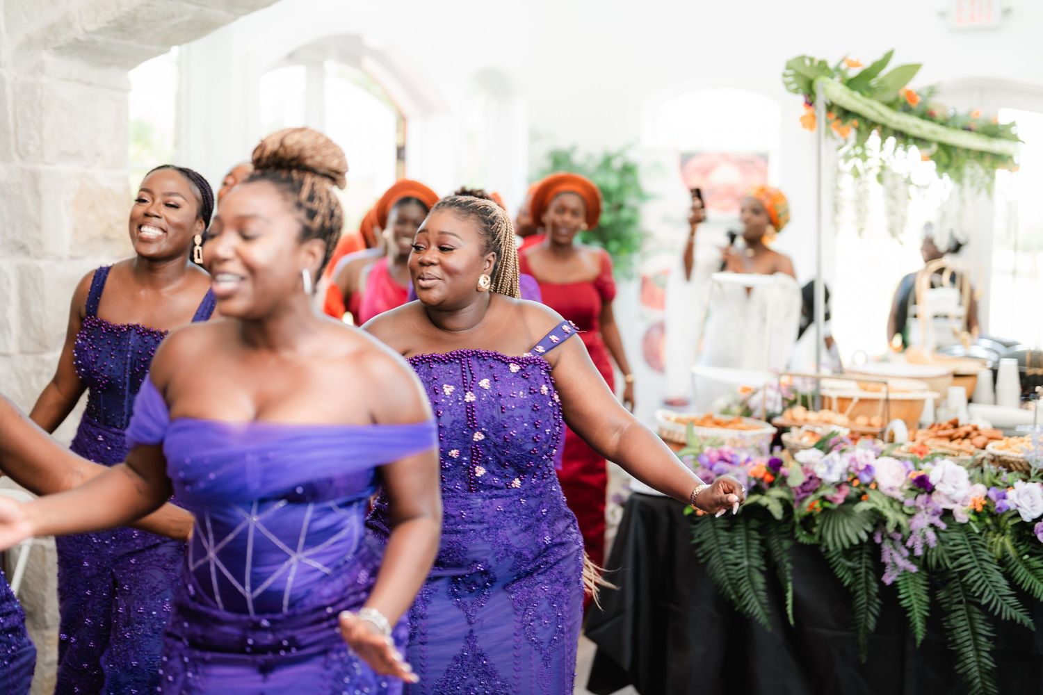 Wedding party wearing vibrant purple bridesmaid dresses dancing and celebrating at an outdoor reception.