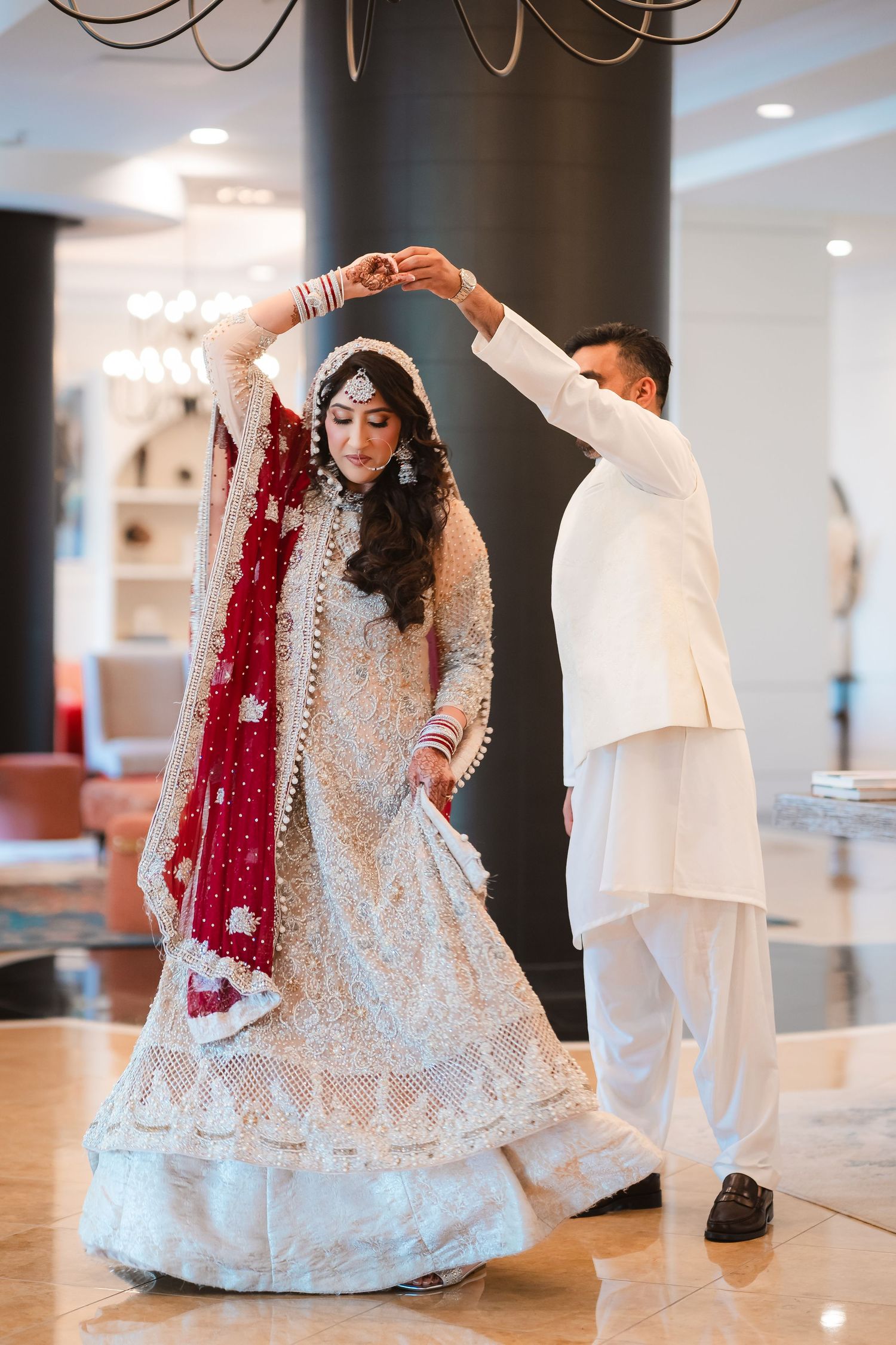 Traditional South Asian wedding ceremony with ornate white lehenga and deep red dupatta in an elegant indoor setting.