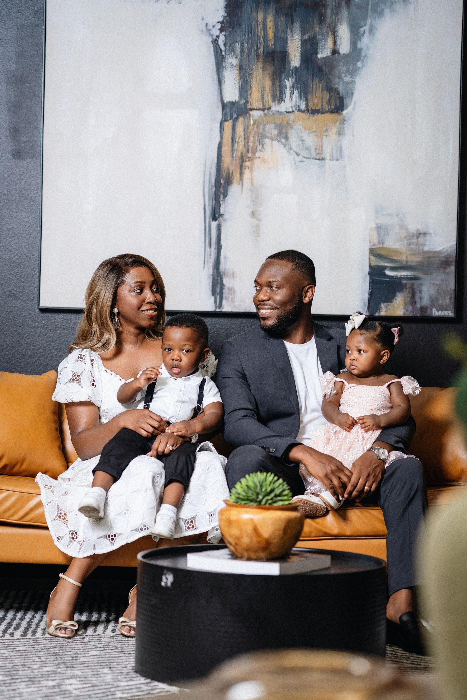 A family relaxes together on a brown leather couch in a modern living room with abstract art on the wall.
