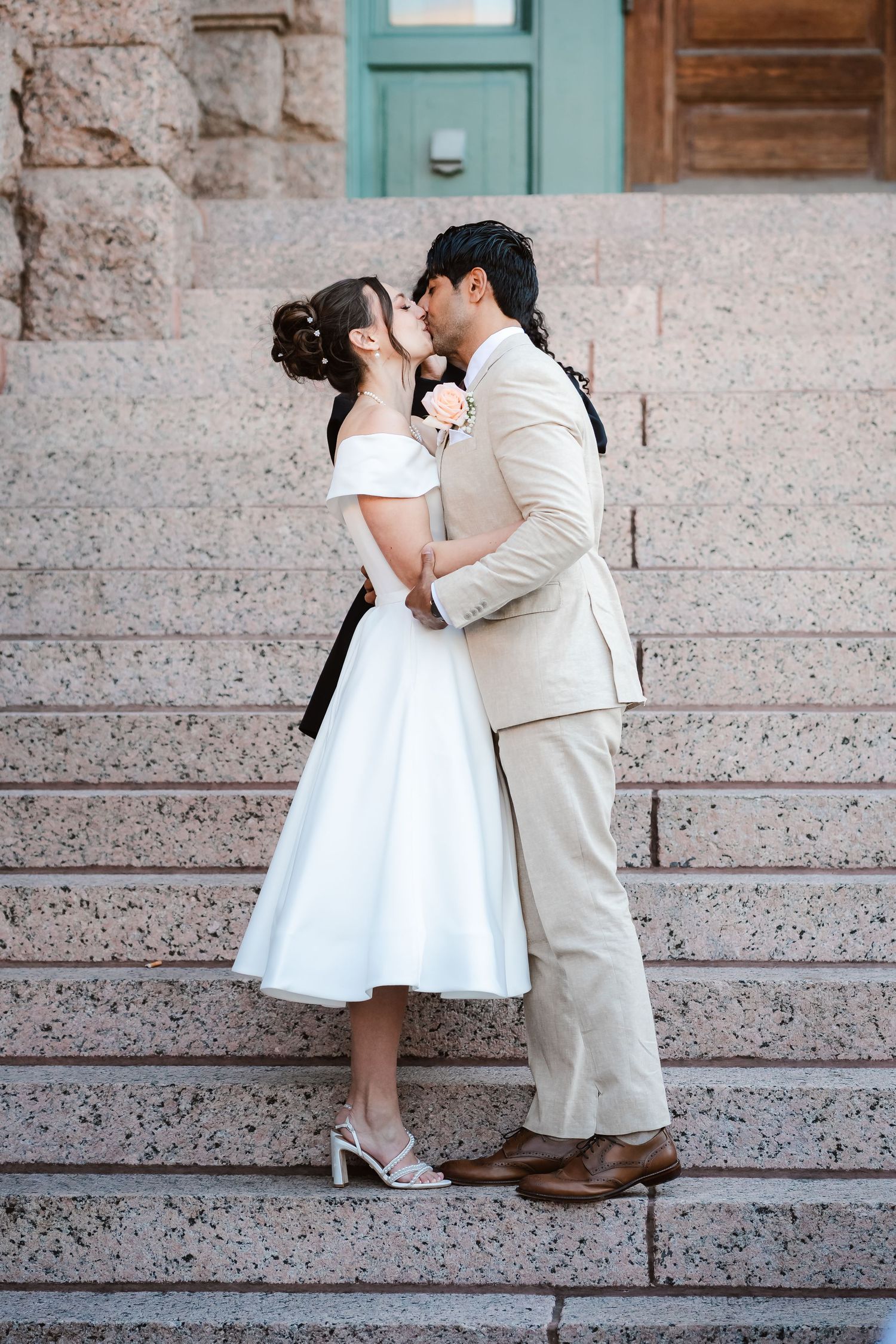 A couple in wedding attire shares a romantic moment on stone steps.