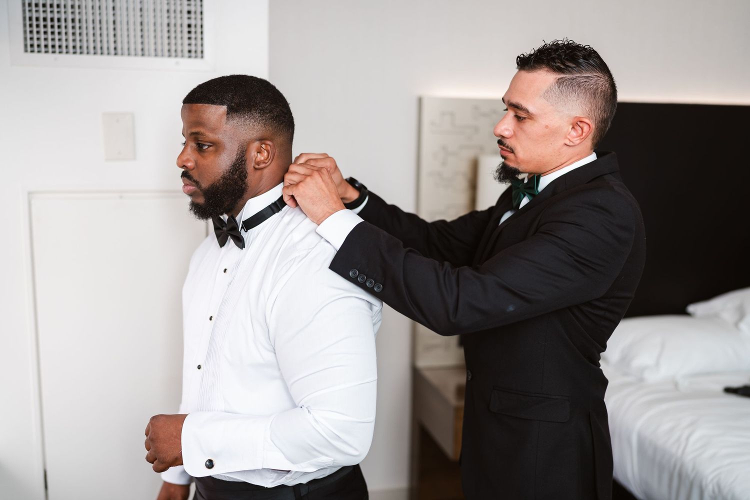 Groomsmen helping with formal attire preparations in a bright room.